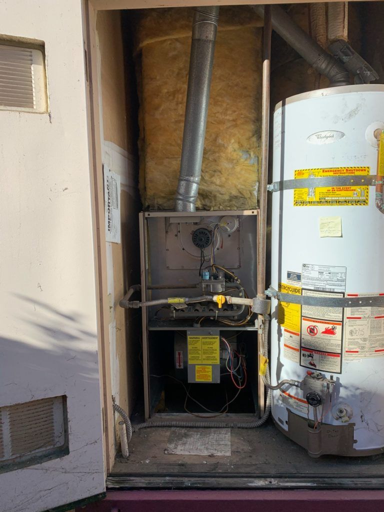 Furnace and water heater in an outdoor utility closet; vent pipe, insulation visible.