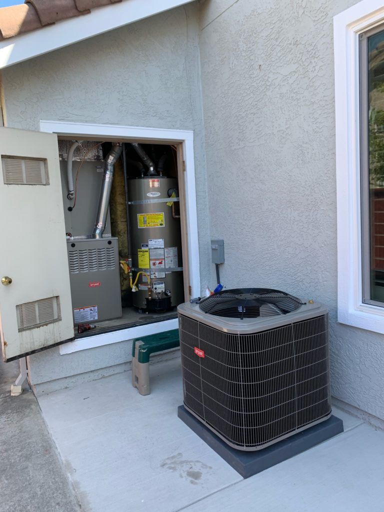 HVAC system on a patio. Air conditioner unit outside, furnace and water heater inside a wall-mounted enclosure.