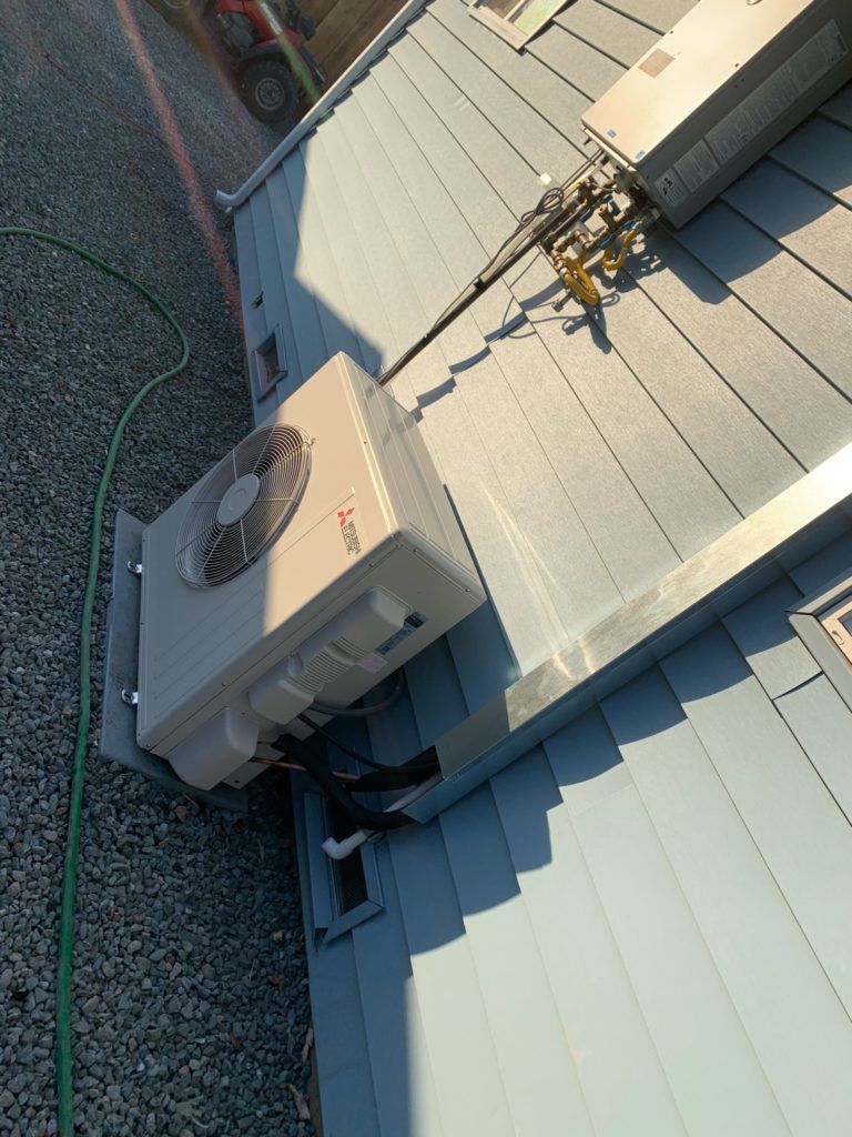 An air conditioning unit mounted on a blue shingled roof with a gravel driveway nearby.