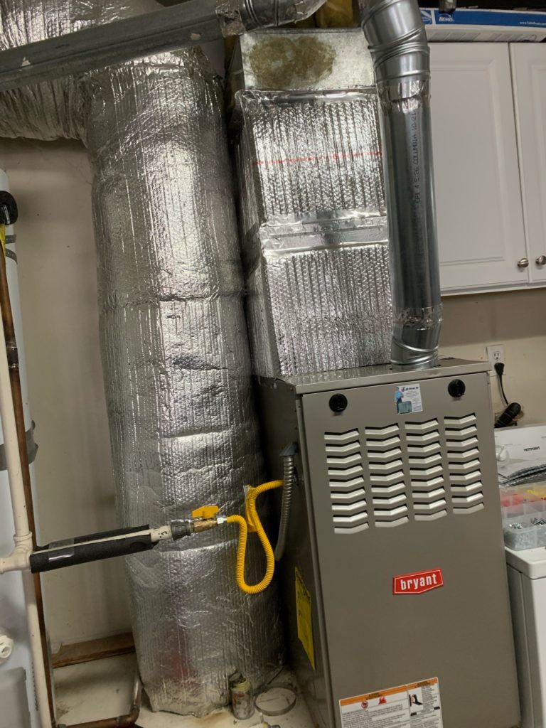 HVAC furnace unit with insulated ductwork. Silver and gray, in a utility room.