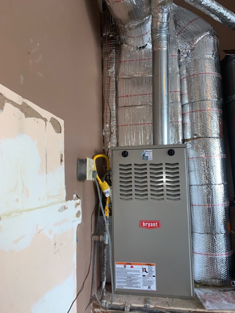 A Bryant furnace installed against a wall with ductwork; gray and silver colors dominate.