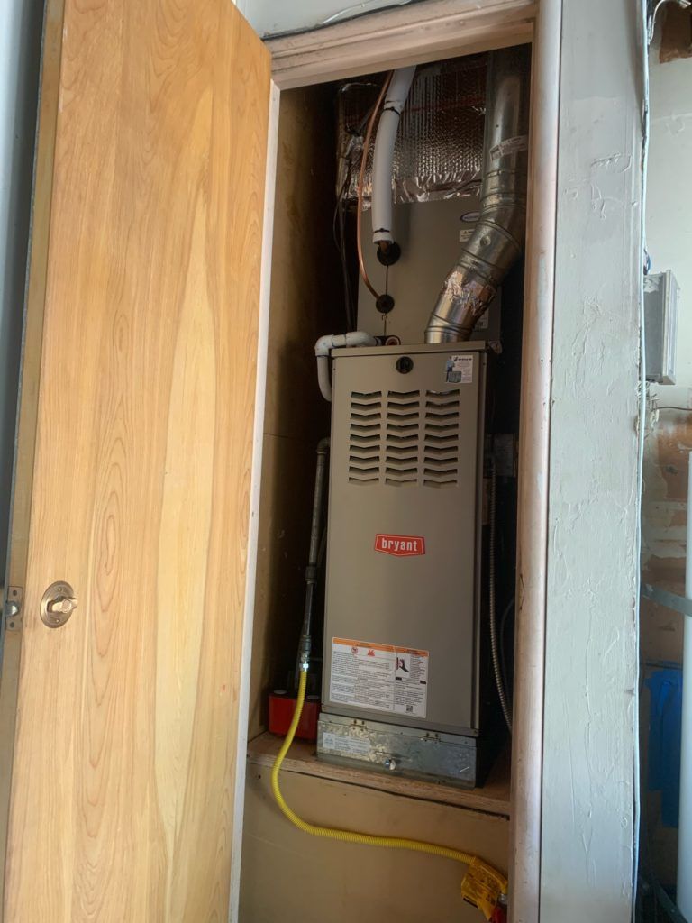 Furnace unit inside a wooden-framed closet. A door is ajar, with a yellow extension cord running out.
