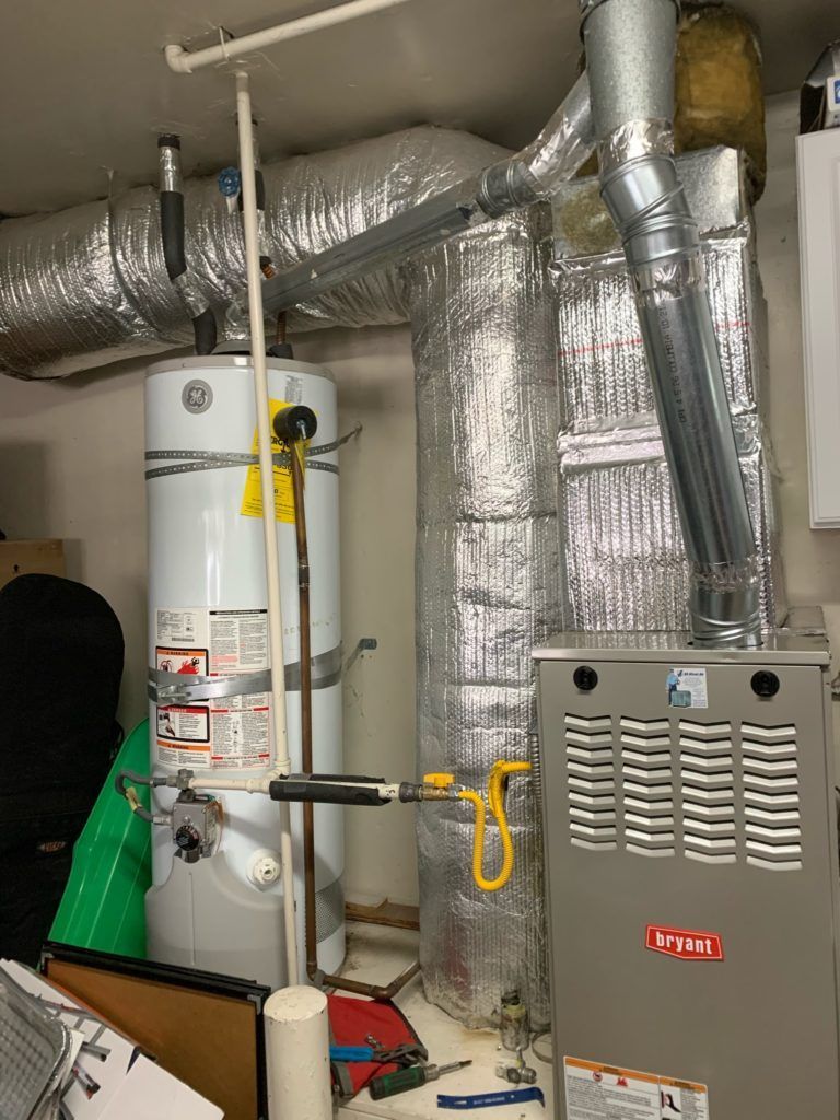 Water heater, furnace, and ductwork in a utility room. Silver insulation, metallic vents, and white water tank.
