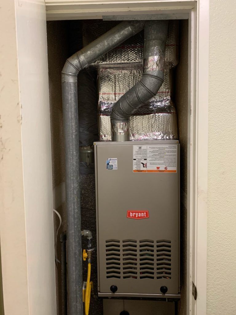 Furnace unit inside a closet, Bryant brand. Silver ducts and insulated wrapping visible.