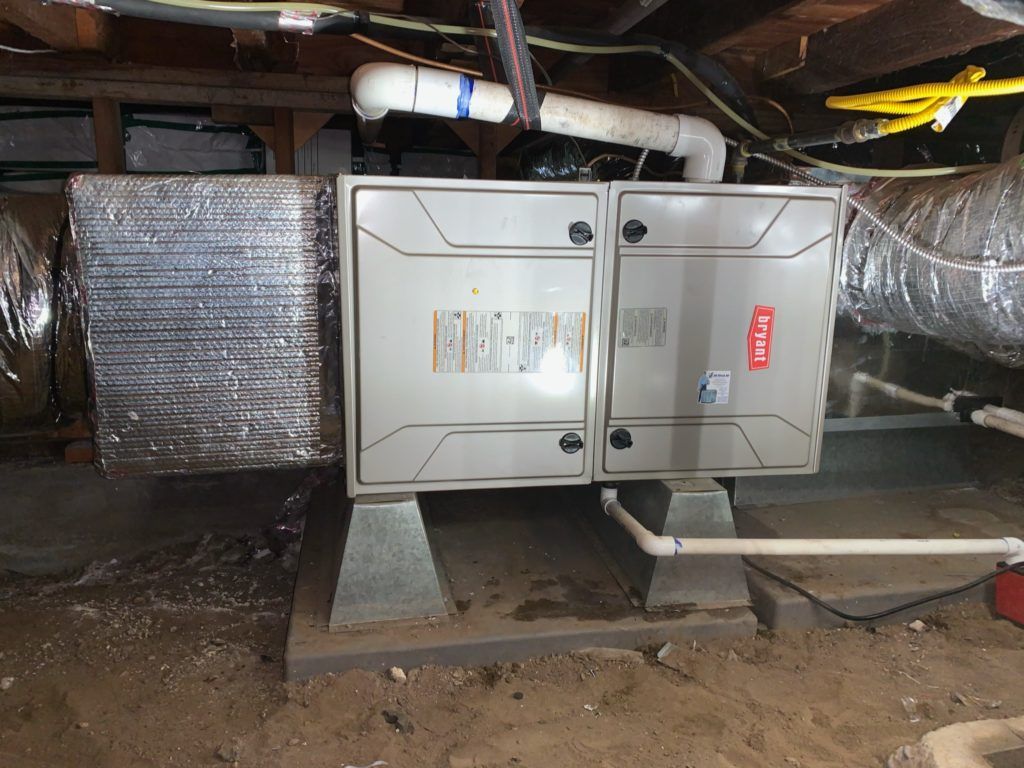 HVAC unit on concrete blocks in a basement. Ductwork and pipes visible.