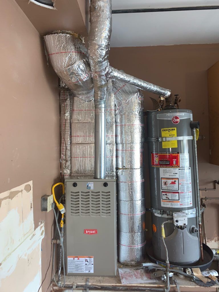 A furnace and water heater are in a utility room. Ductwork is wrapped with insulation.