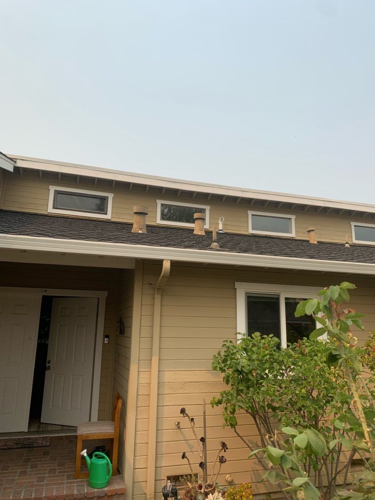 Tan house exterior with a row of small windows, visible vents, and a partially open door.