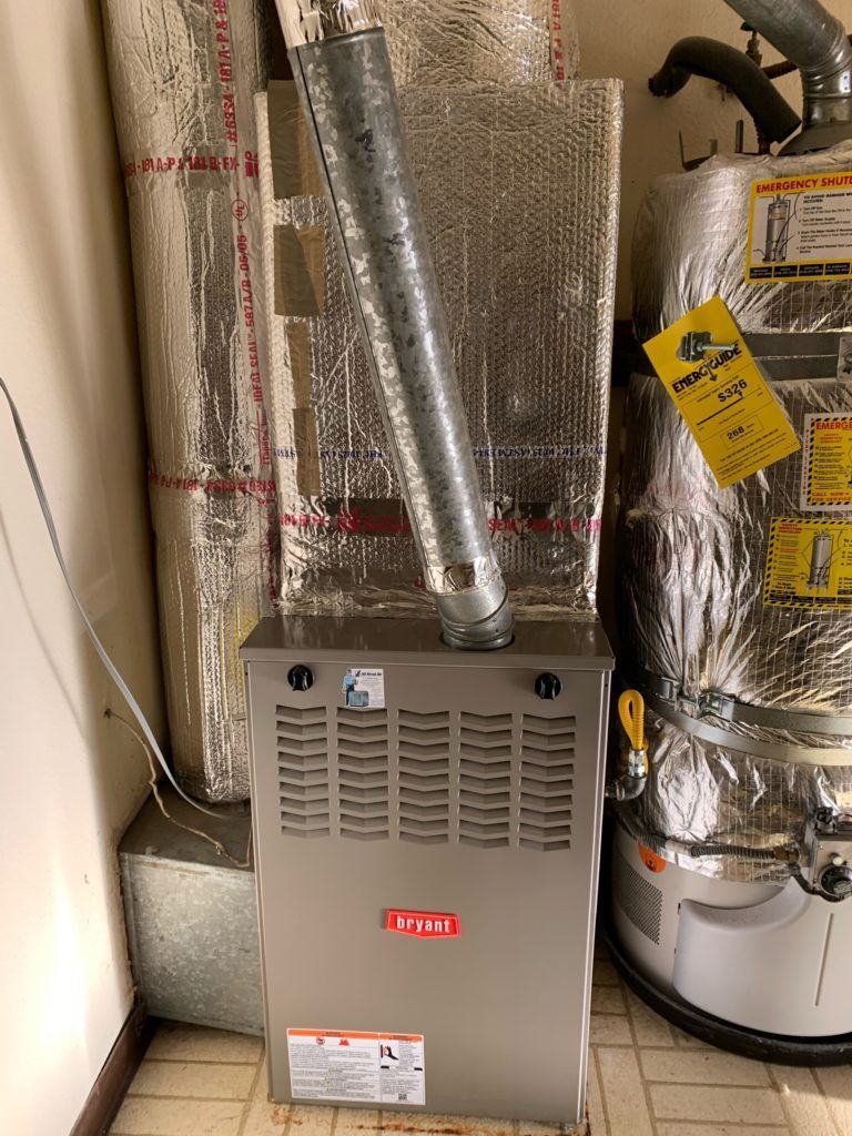 Furnace with ductwork and a water heater in a utility room. Gray and silver colors.