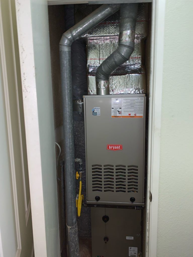 Furnace unit in a closet with ductwork and a gas line.