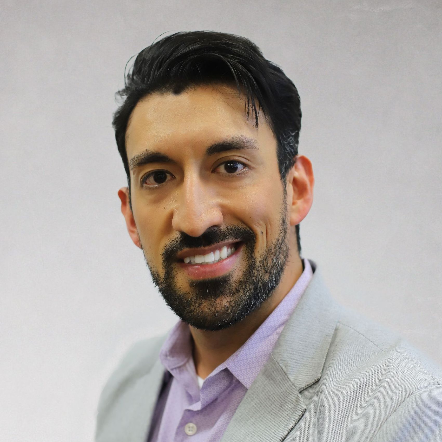 A man with a beard is wearing a suit and smiling for the camera.