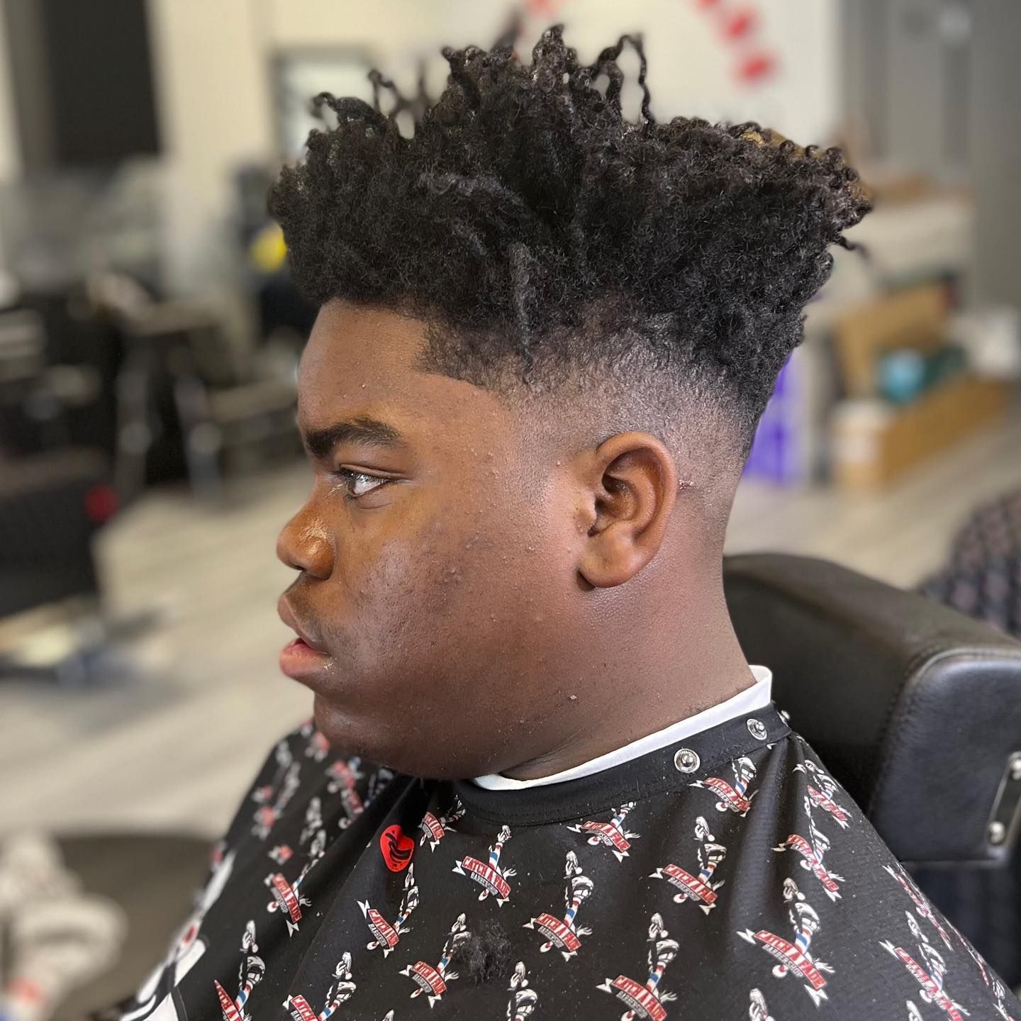 Person with a high-top fade haircut, sitting in a barber chair.