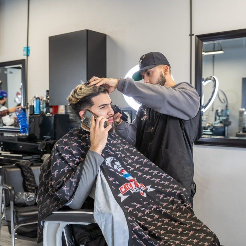 A barber giving a haircut to a client talking on the phone in a salon.
