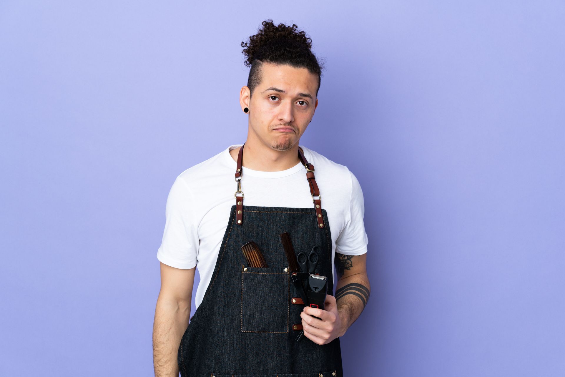Person in denim apron, holding scissors, looking at the camera.
