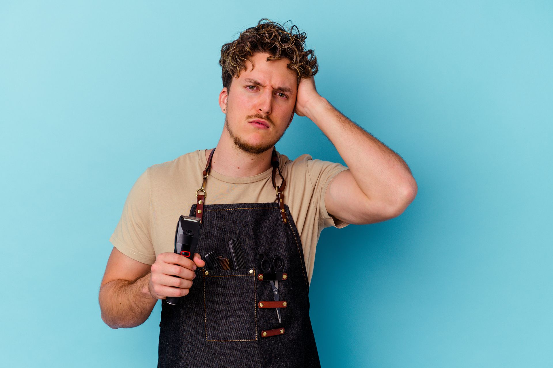 Man in barber apron holding clippers, looking stressed, against a blue background.