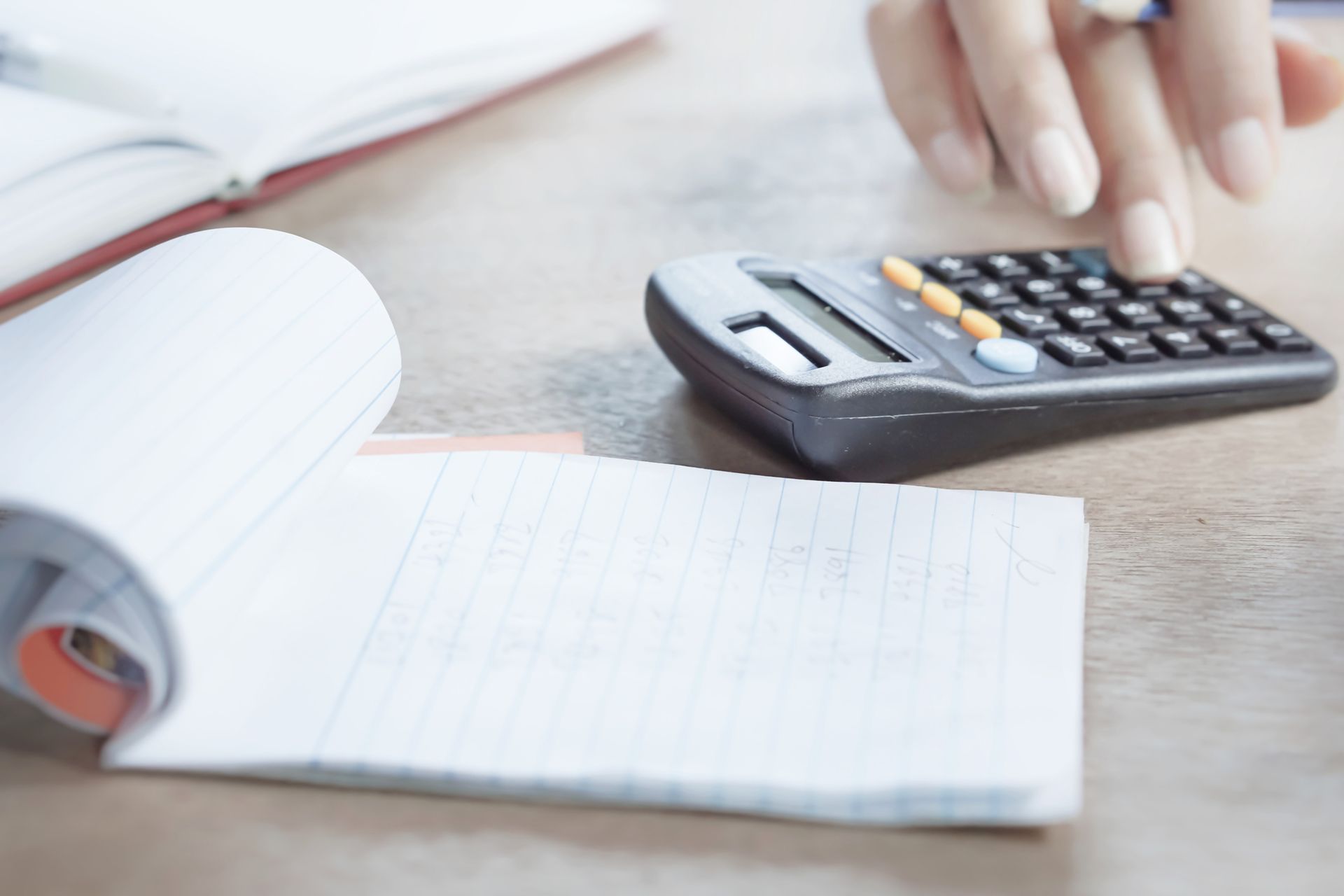 Hand typing on a calculator during tax season with a notebook in the foreground.