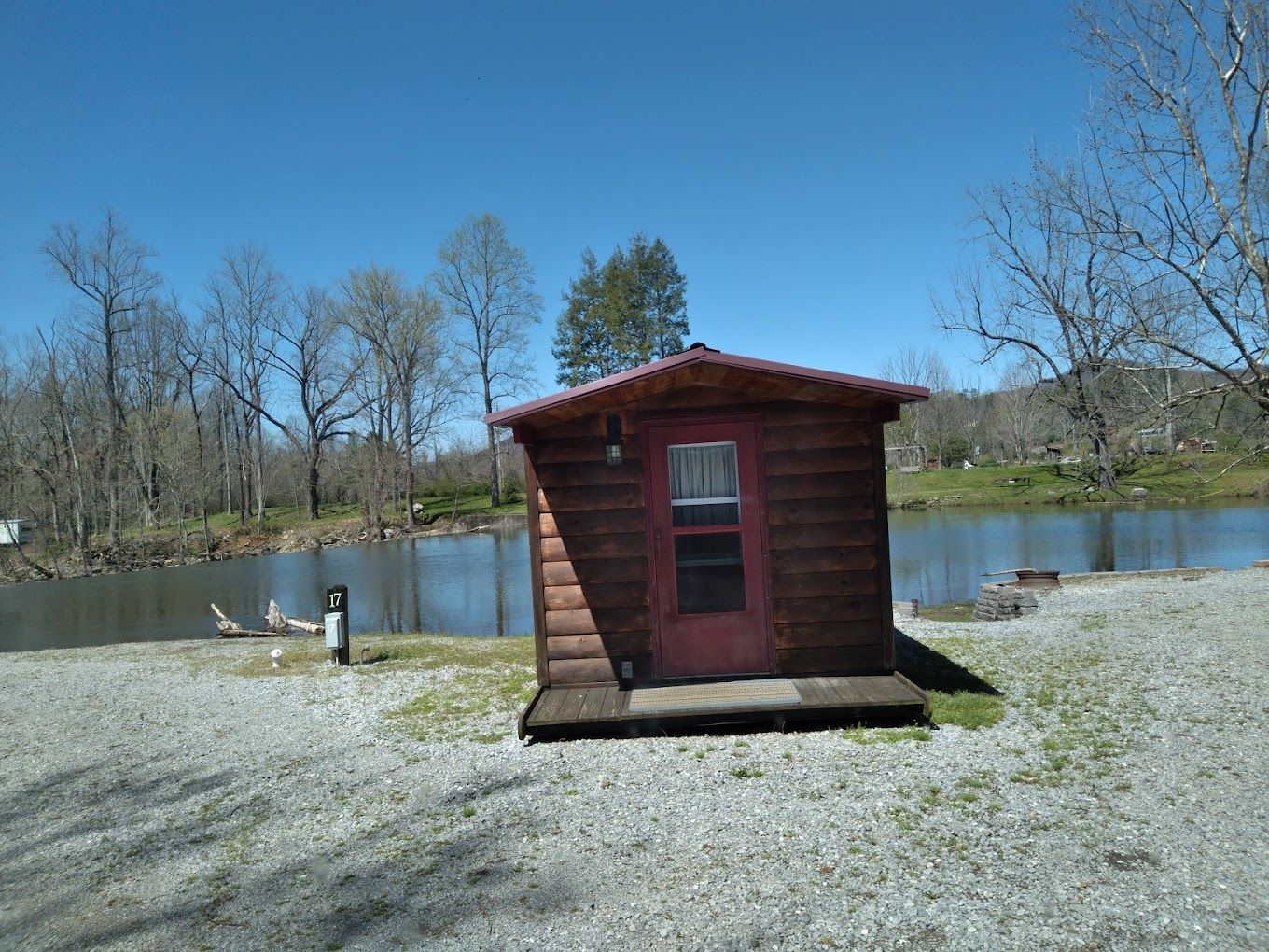A small log cabin with a red door is sitting next to a lake.