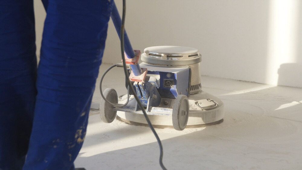 A Person in Blue Work Pants Uses a Floor Sanding Machine — Cyclone City Cleaners In Winnellie, NT