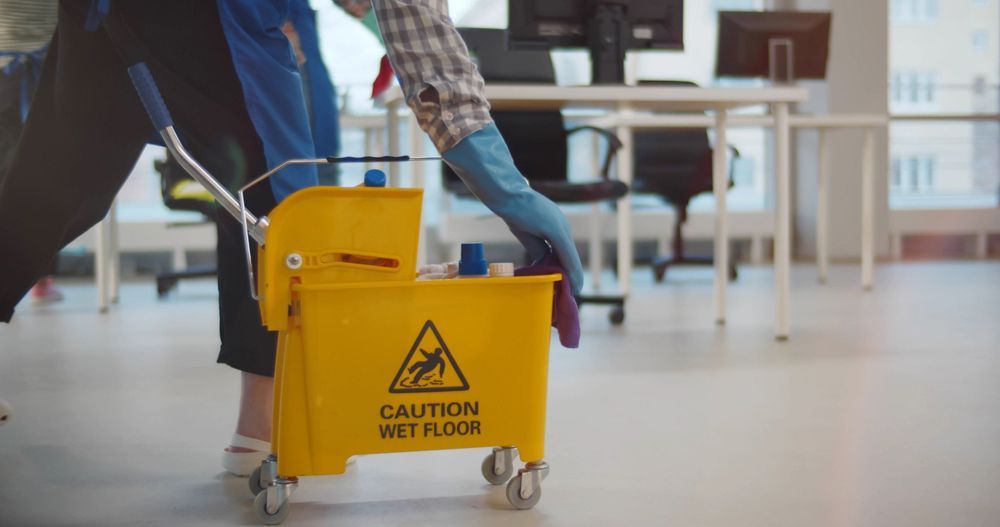 A Cleaner Pushes a Yellow Wet Floor Bucket — Cyclone City Cleaners In Winnellie, NT