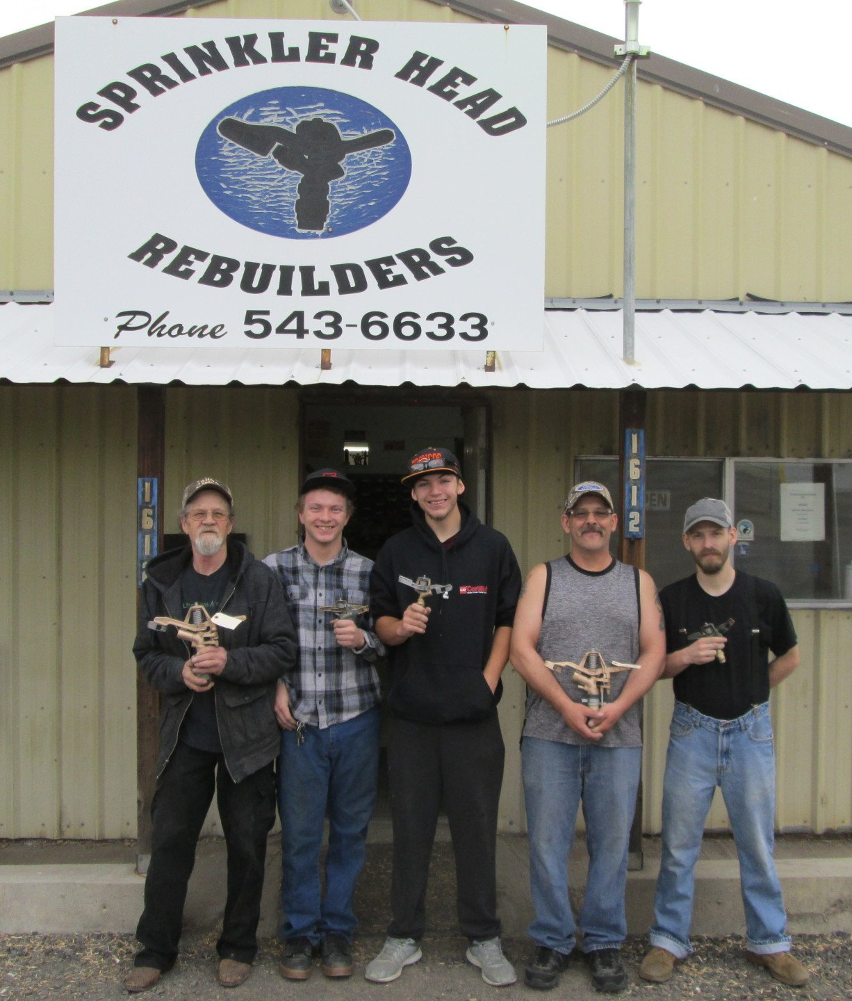 A group of men standing in front of a sign that says sprinkler head rebuilders