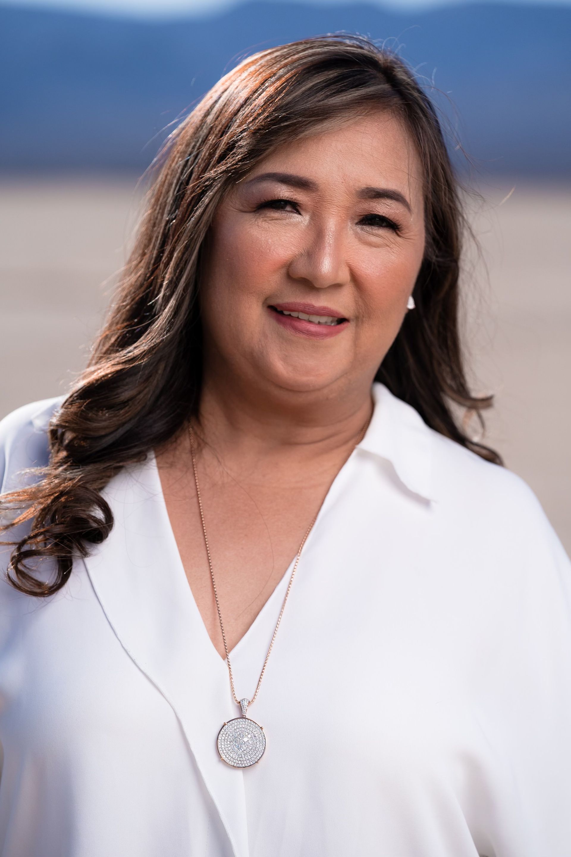 A woman wearing a white shirt and a necklace is smiling for the camera.