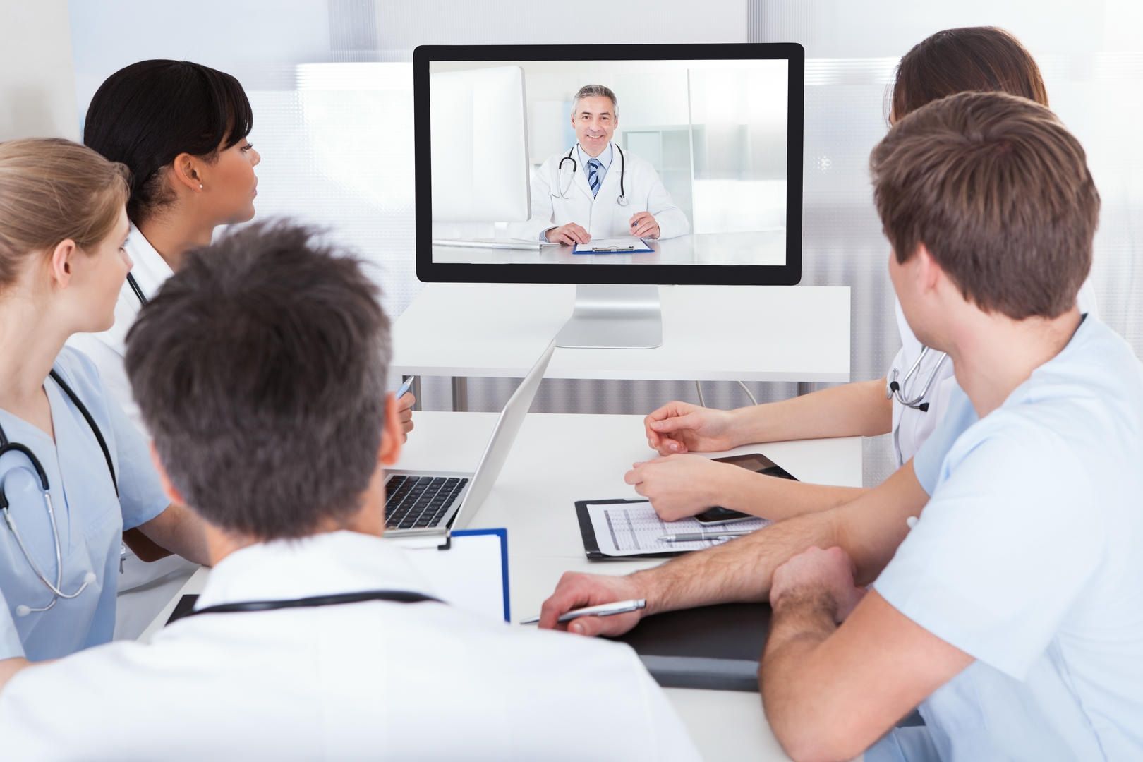 A group of doctors are having a video conference with a doctor on a computer screen.