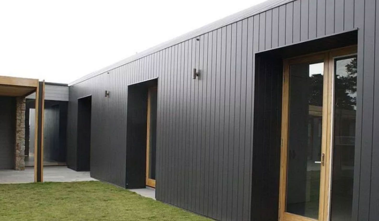 Dark gray building exterior with wooden doors and sconce lighting.