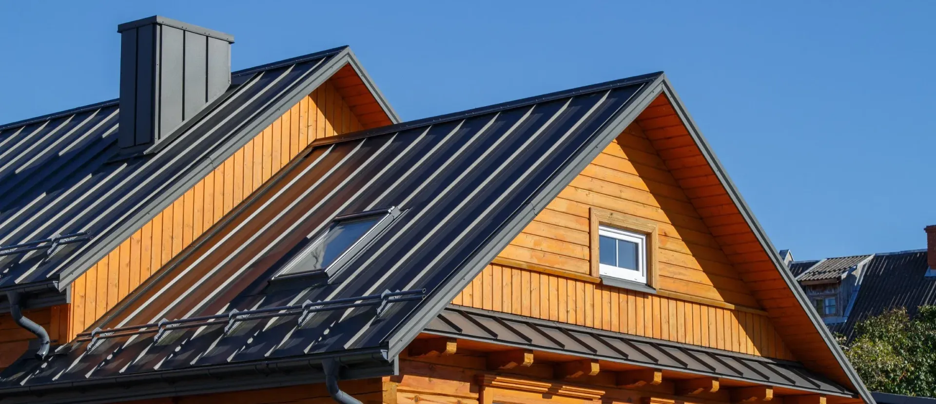 Wooden house roof with dark gray metal roofing against a clear blue sky.