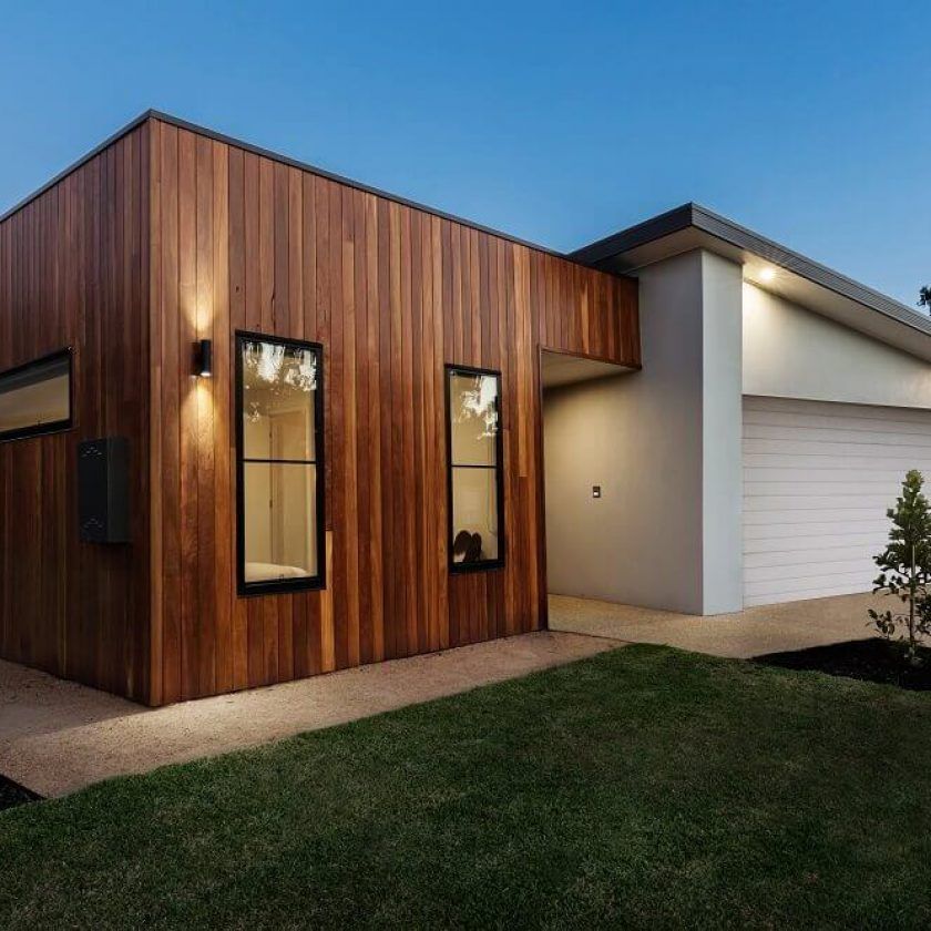Modern house with wood siding, windows, and garage. Green lawn, blue sky.