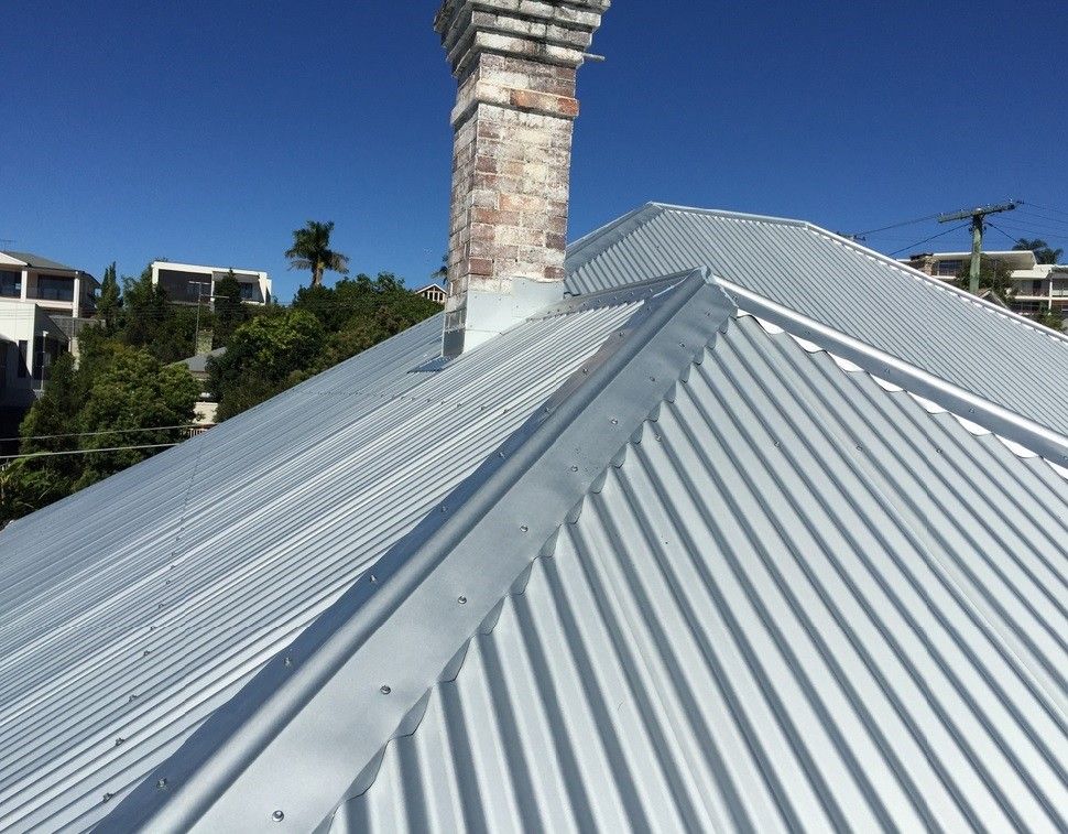 Corrugated metal roof on a building with a brick chimney under a clear blue sky.