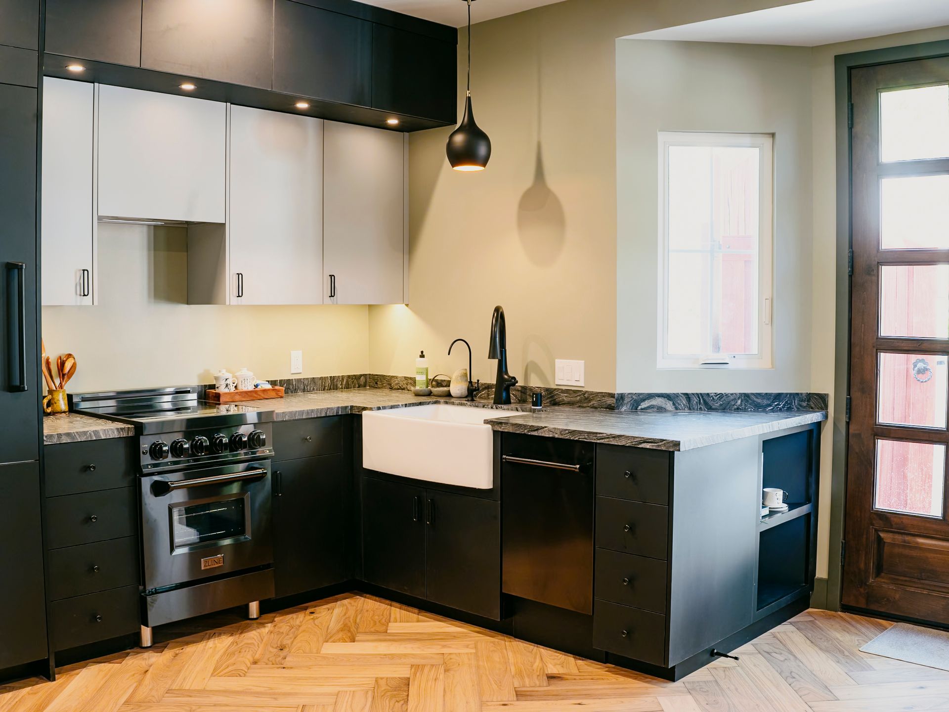 Modern kitchen with black and white cabinets, stainless steel appliances, and herringbone floor.