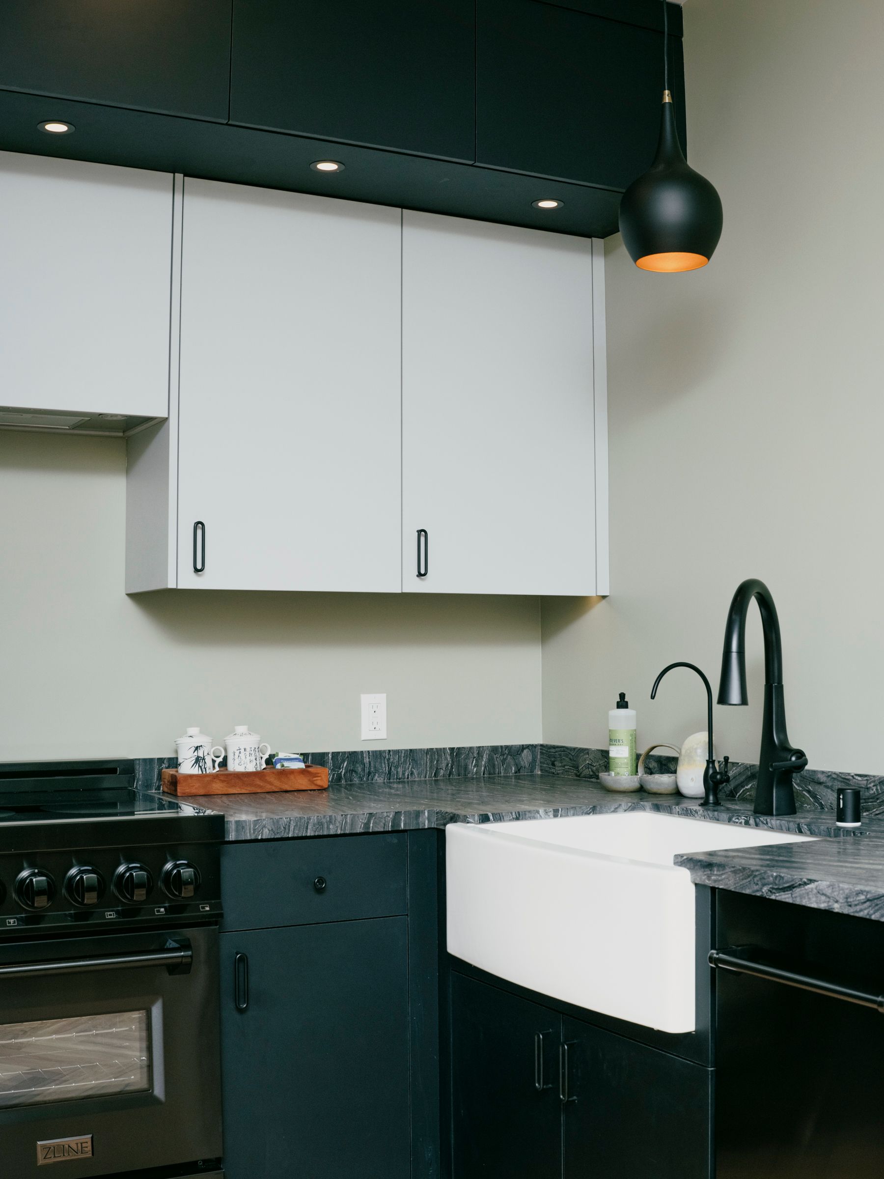 Kitchen with white cabinets, black countertop, sink, and stove. Black light fixture hangs above.