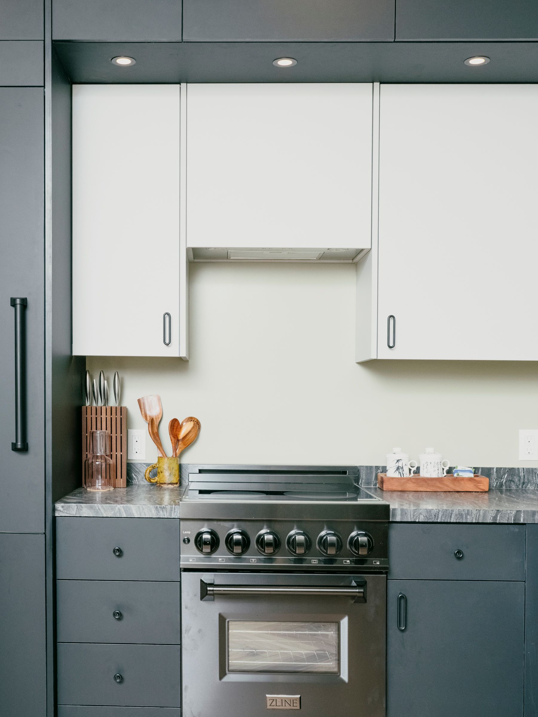 Gray and white kitchen with stainless steel range, grey cabinets, white upper cabinets, and under-cabinet lighting.