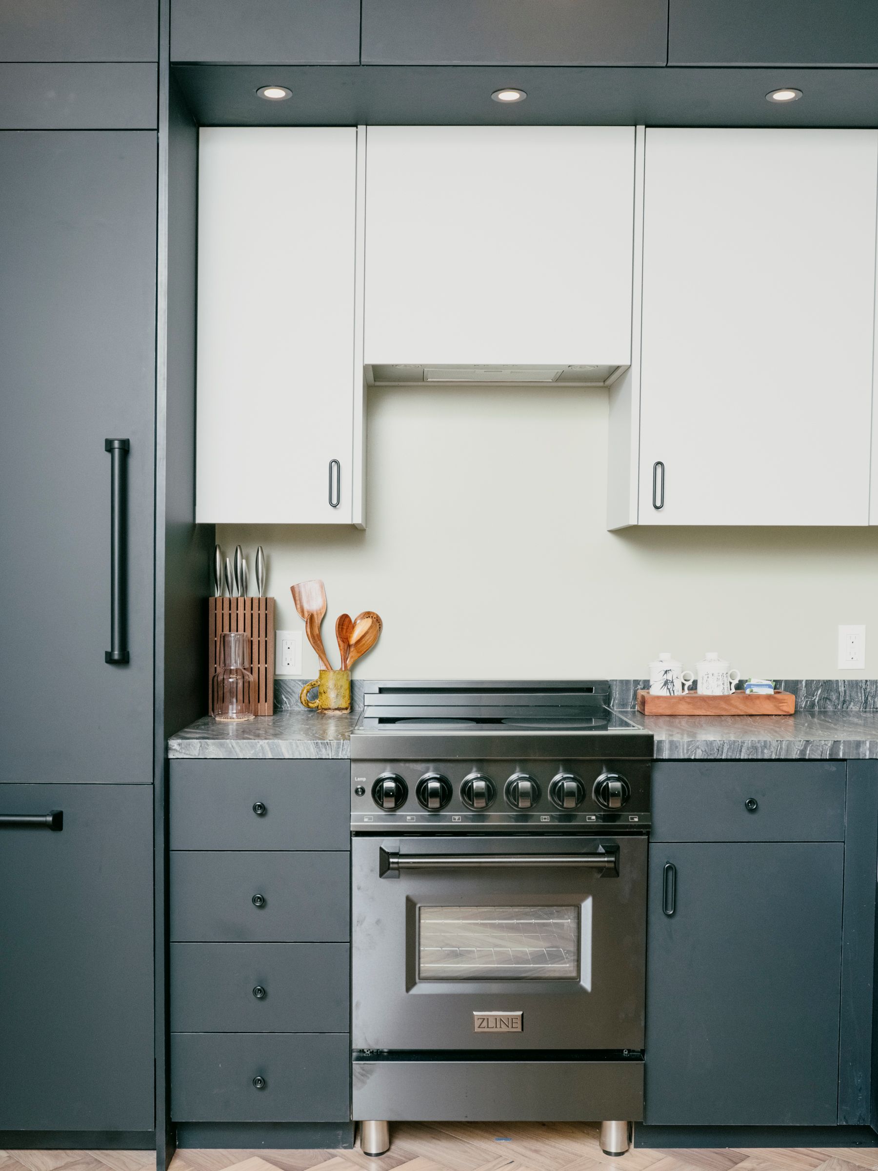 Modern kitchen with stainless steel stove, dark gray cabinets, and white upper cabinets.
