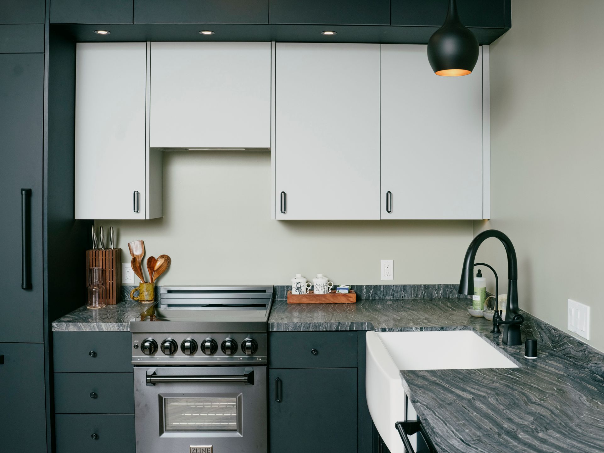 Modern kitchen with gray-blue cabinets, stainless steel stove, granite countertops, and white sink.