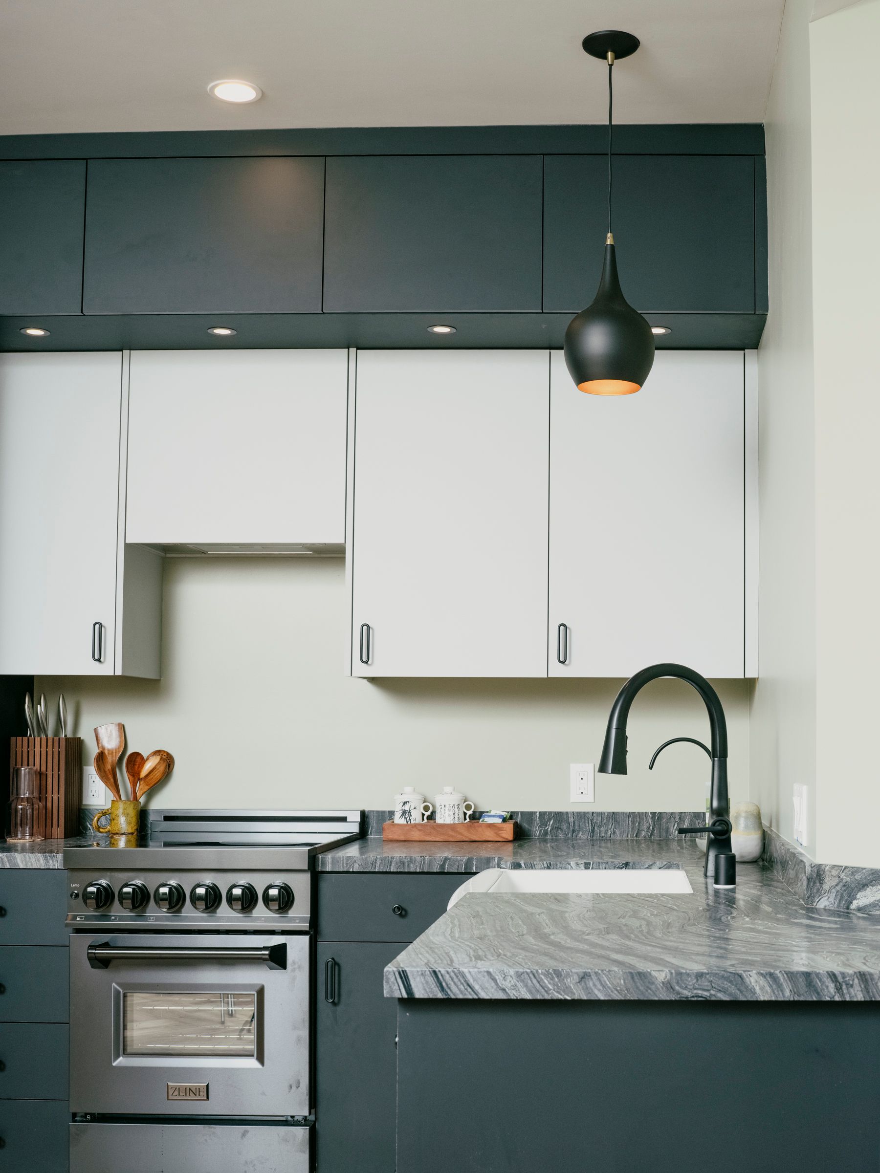 Kitchen with dark gray and white cabinets, stainless steel appliances, and black pendant light.