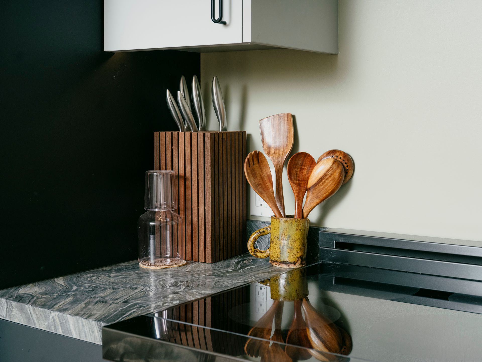 Kitchen countertop with wooden utensils, knives, and a glass carafe.