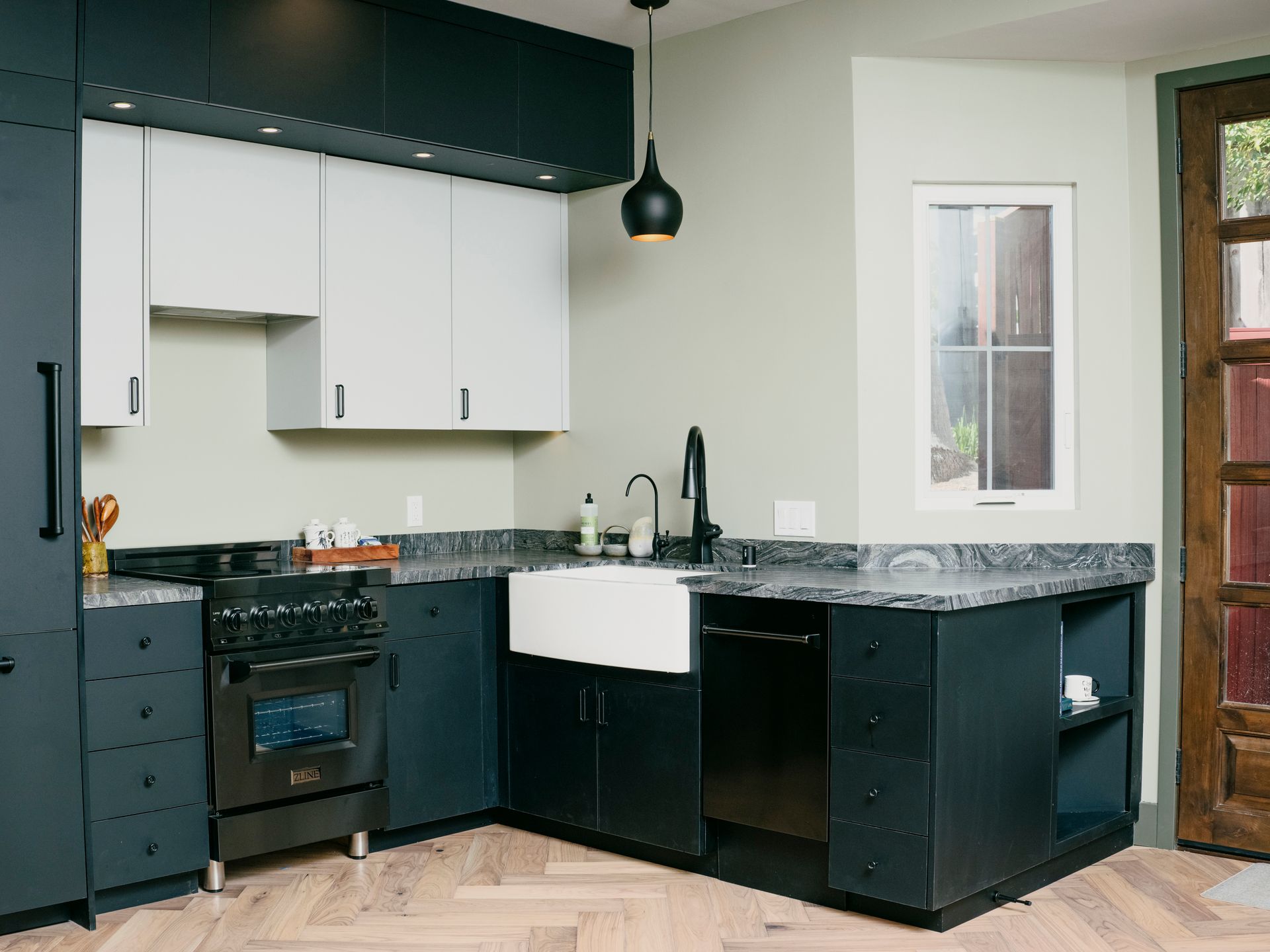 Modern kitchen with dark blue cabinets, light countertops, white farmhouse sink, and a small window.