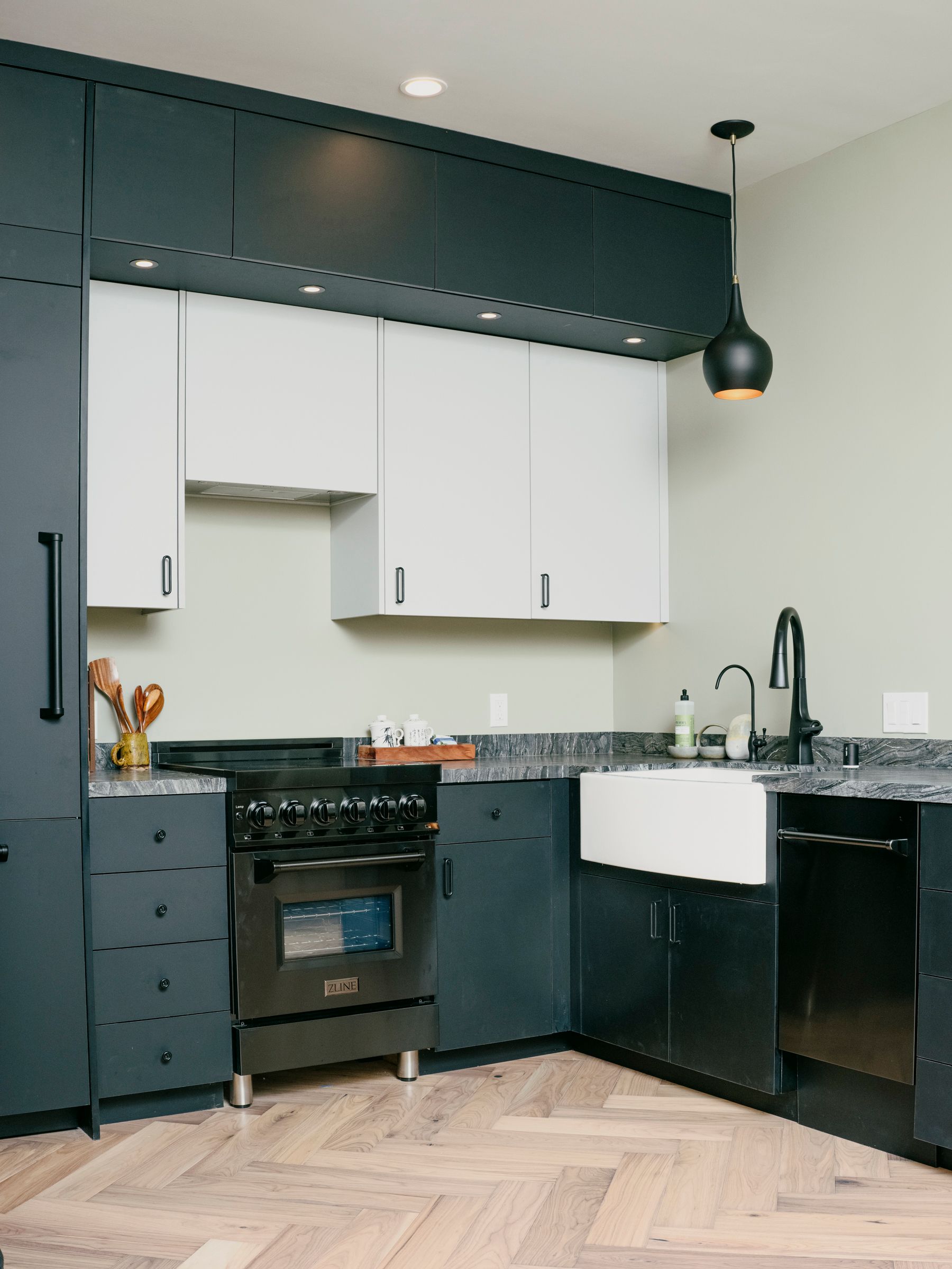 Modern kitchen with black and white cabinets, farmhouse sink, black appliances, and herringbone floors.