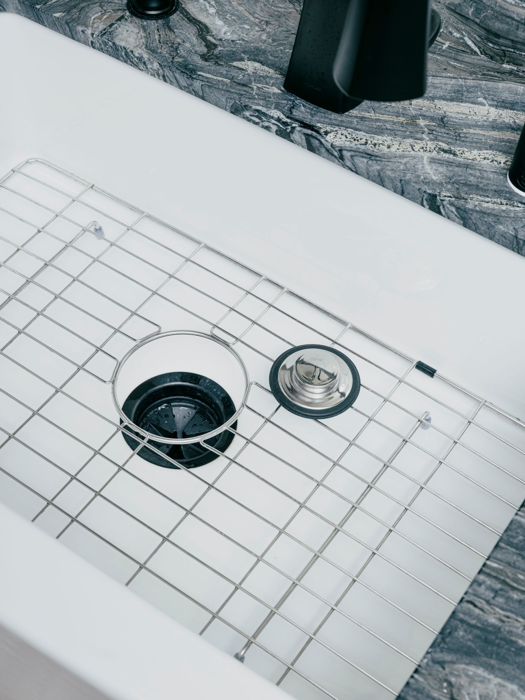 White kitchen sink with metal grid over the drain, black drain and faucet.