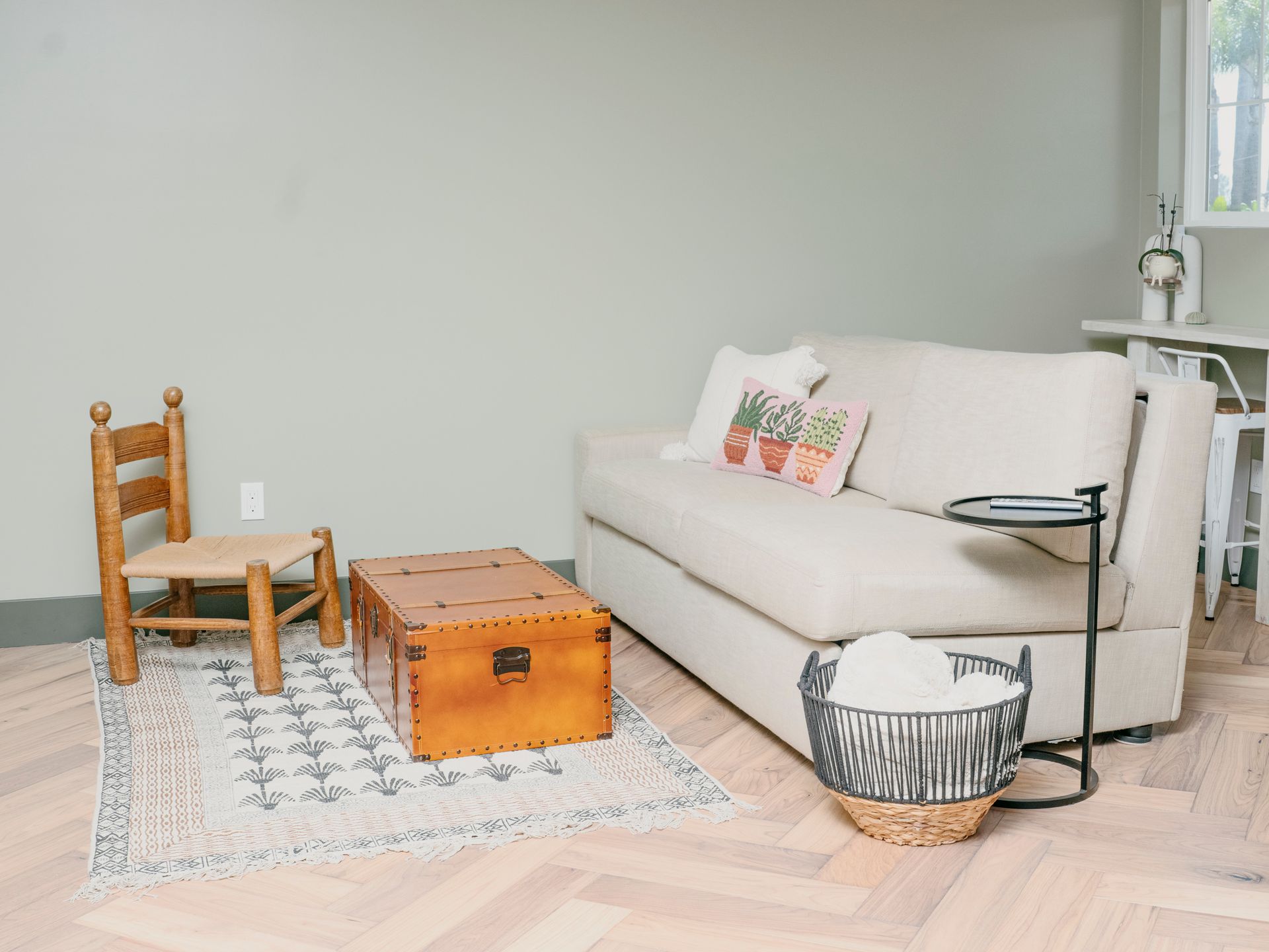 Cozy living space: Cream sofa, brown trunk, small chair, patterned rug, and black side table.