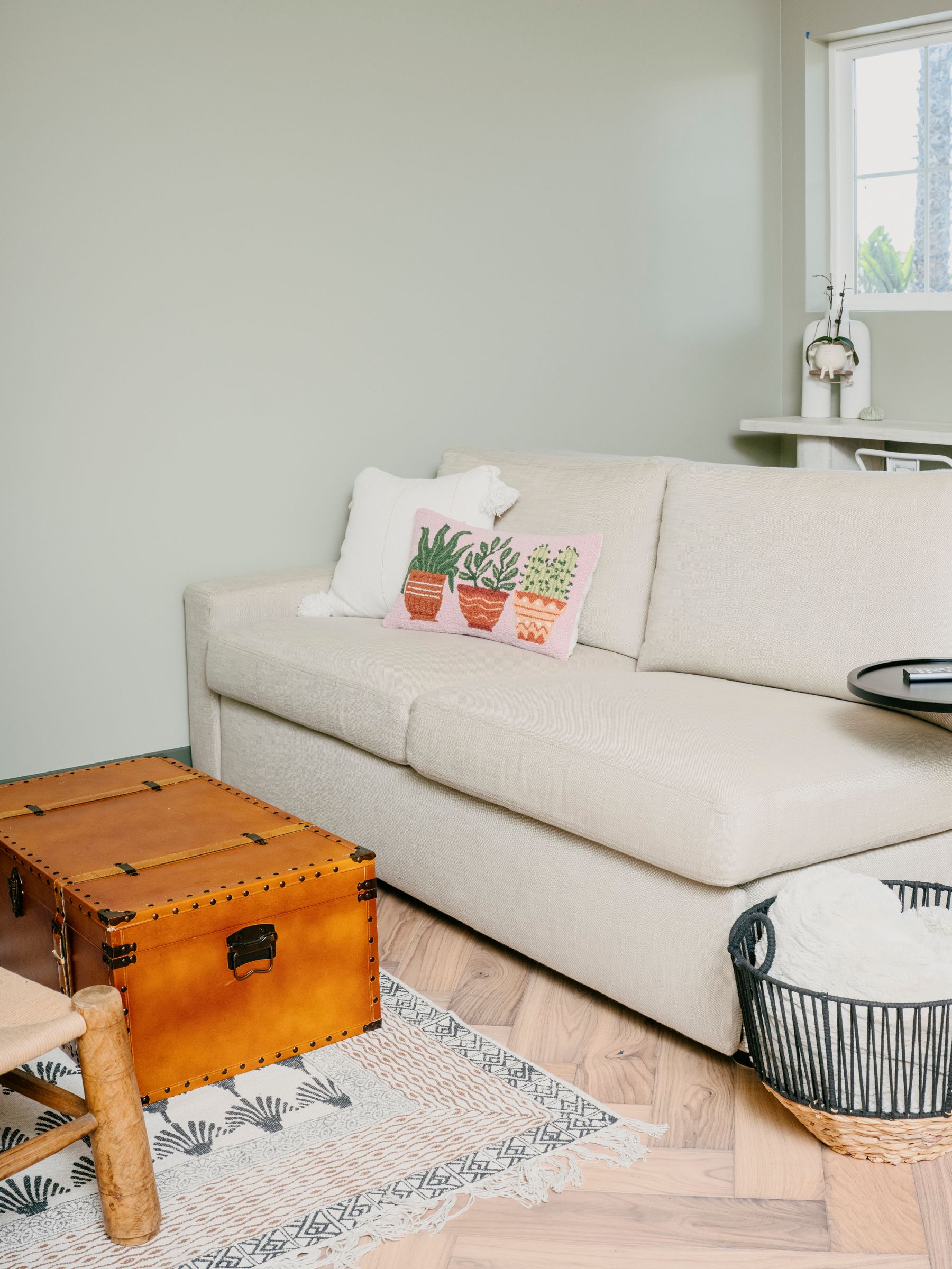 Cozy living room with a cream-colored couch, leather trunk, and cactus-themed pillow.