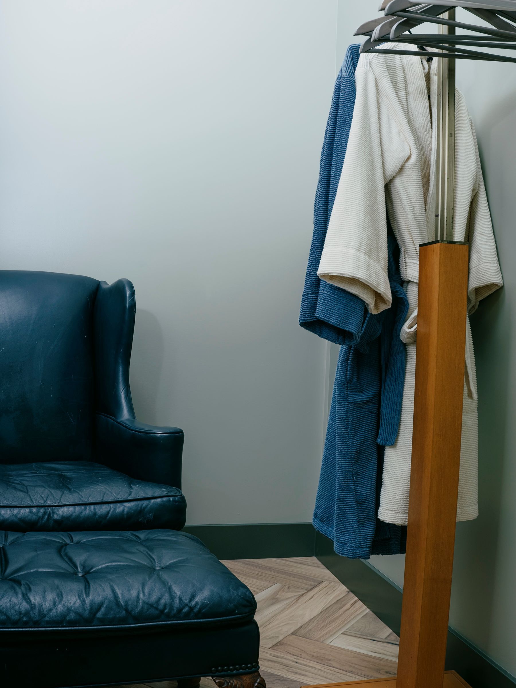 Blue leather armchair and ottoman beside a wooden robe stand with blue and white robes hanging on it.