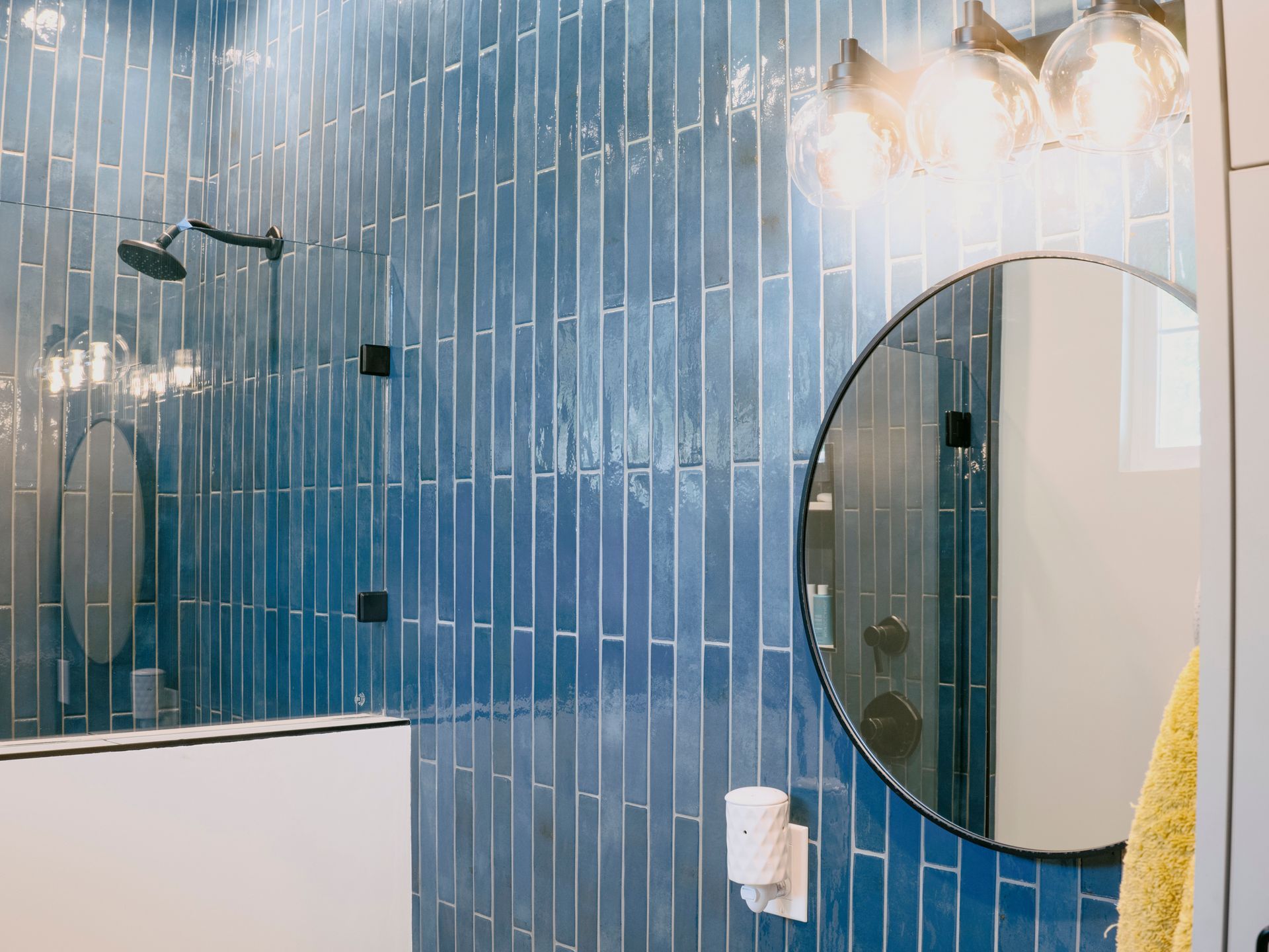 Blue tiled shower with round mirror, clear lights, and black showerhead.