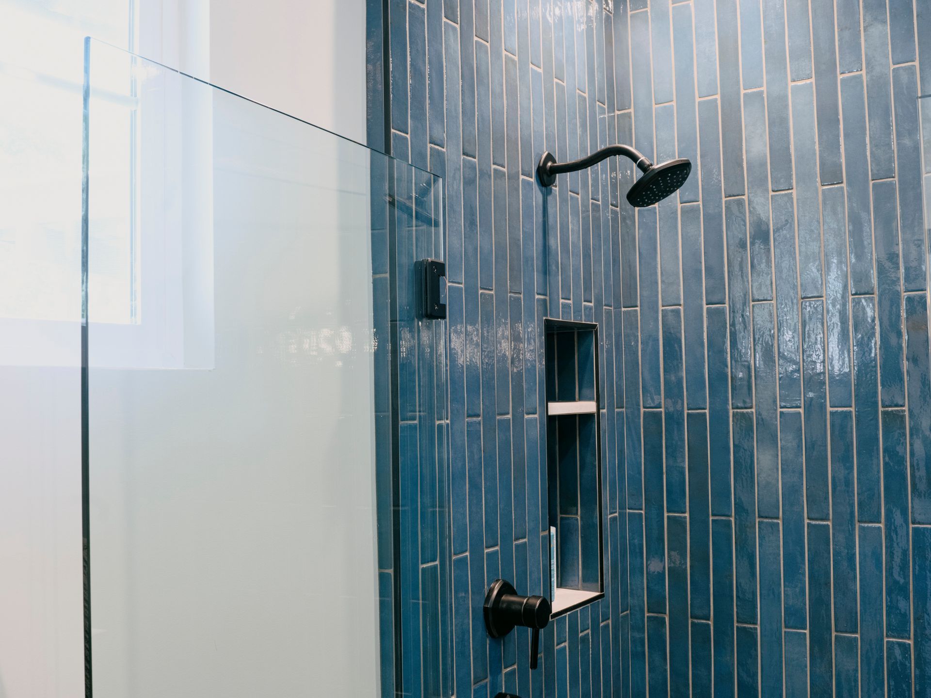 Blue tiled shower with black fixtures and glass door.