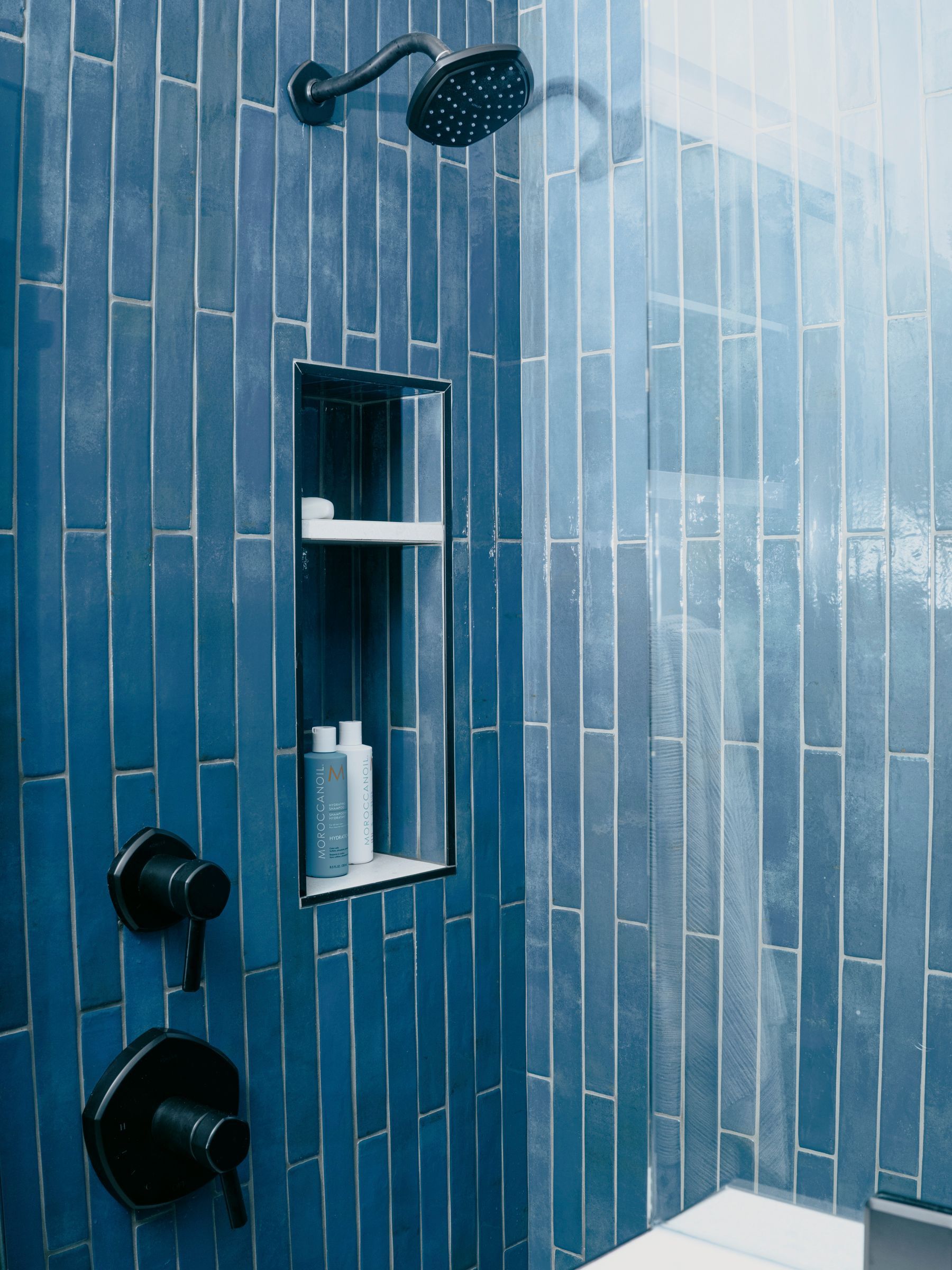Blue tiled shower with black fixtures and a recessed shelf.