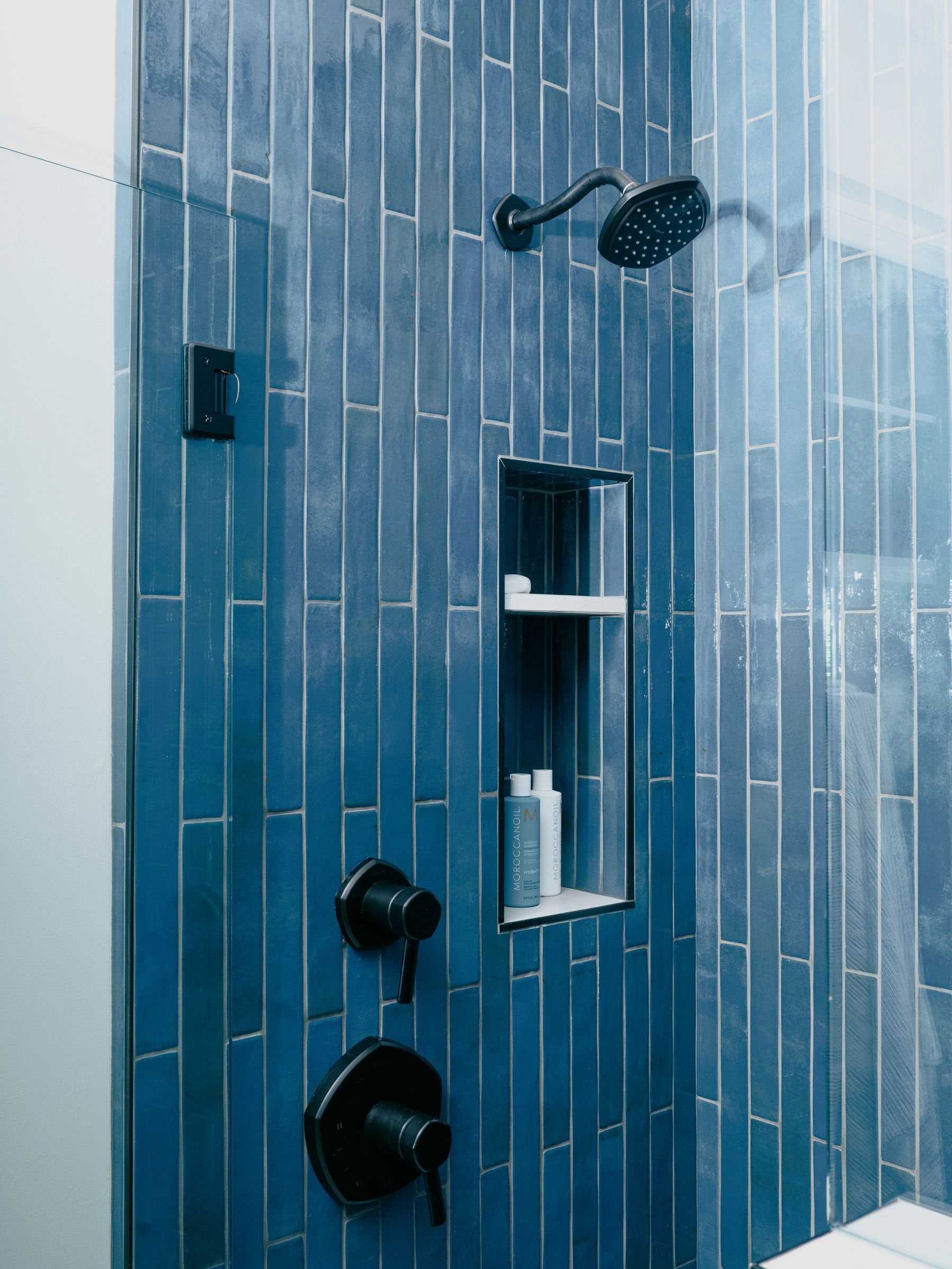 Blue tiled shower with black fixtures and recessed shelf.