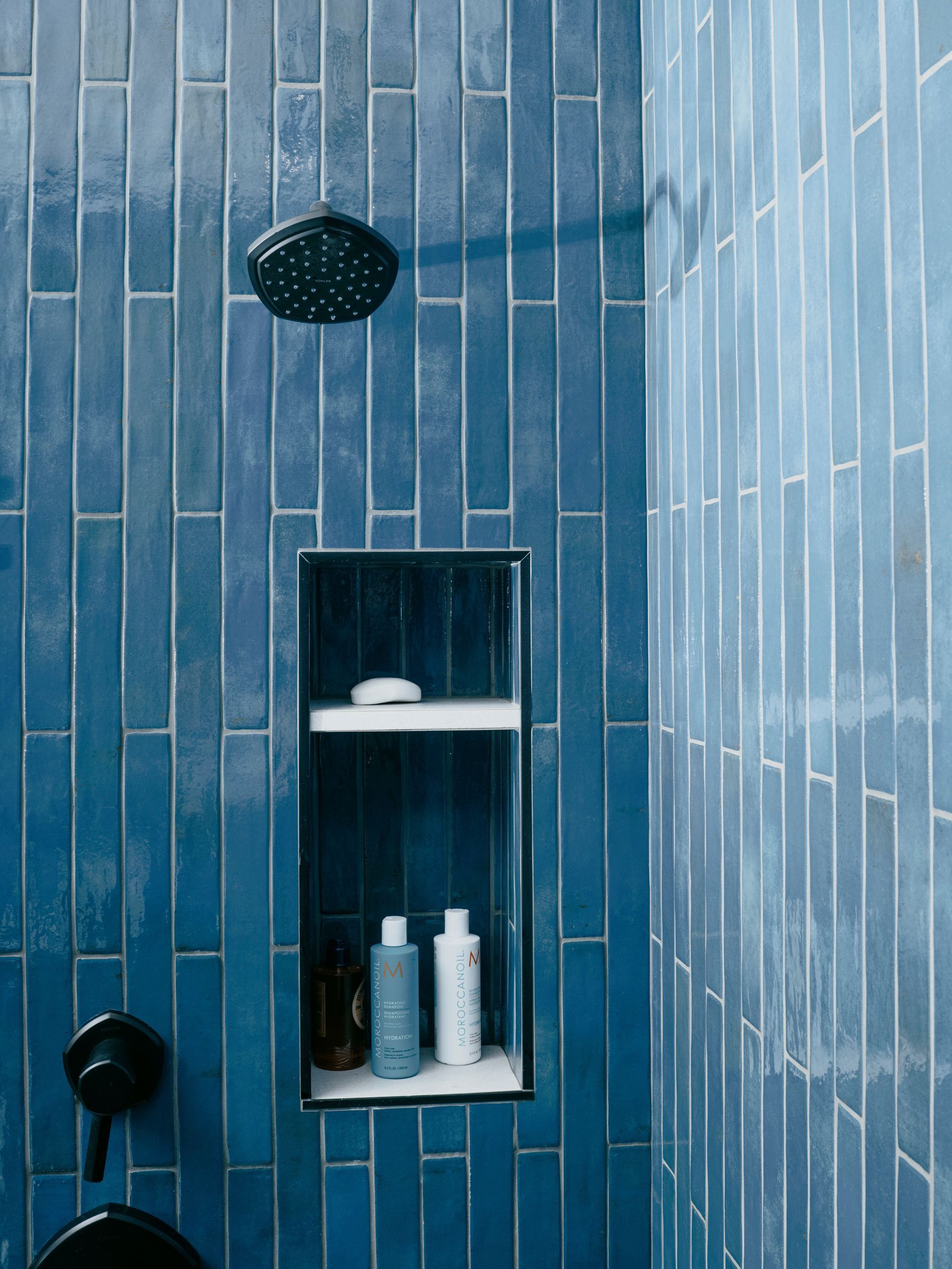 Blue tiled shower with a built-in shelf containing soap and shampoo bottles.