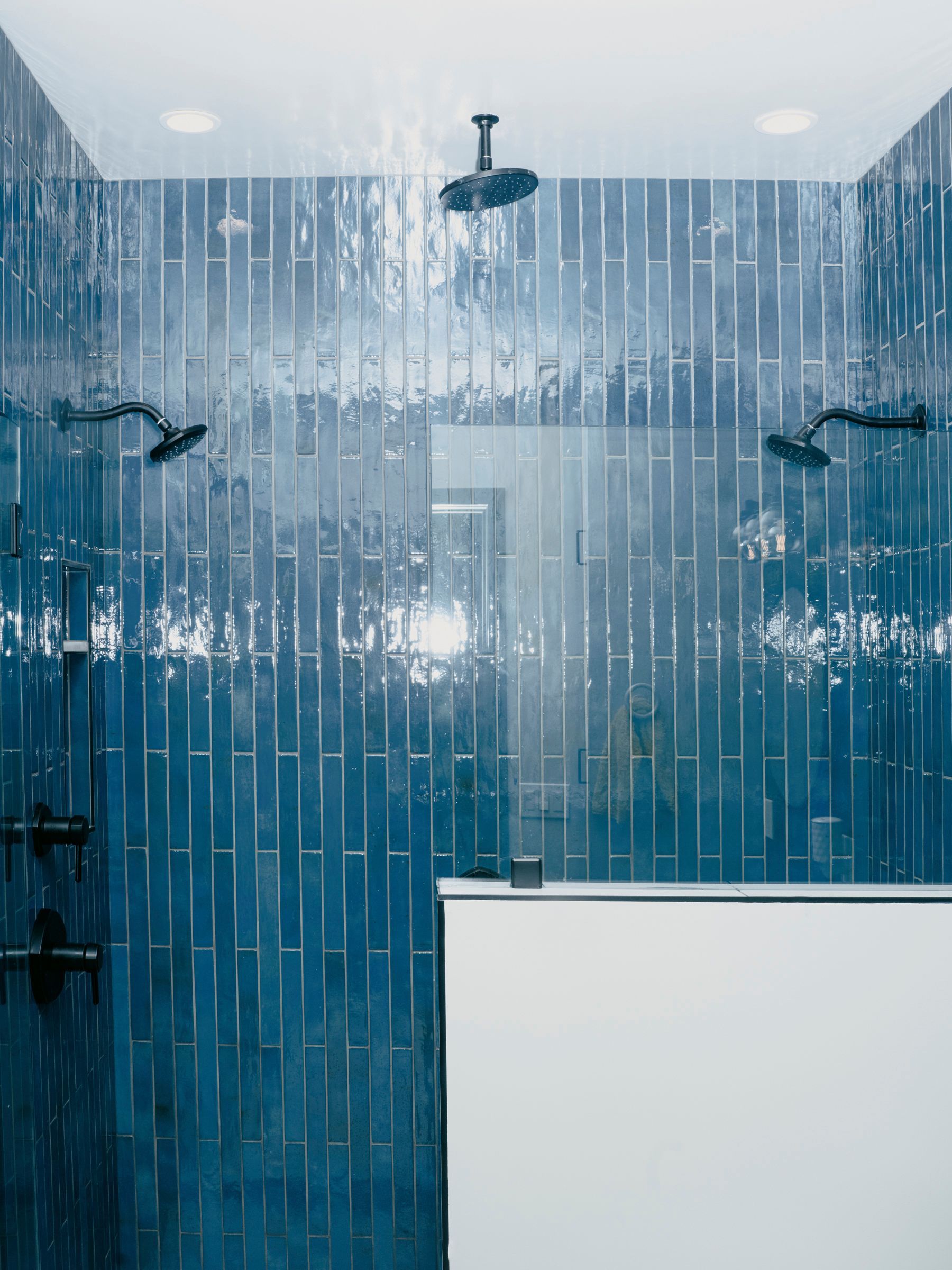 Blue tile shower with multiple showerheads. A glass door is on the right side.