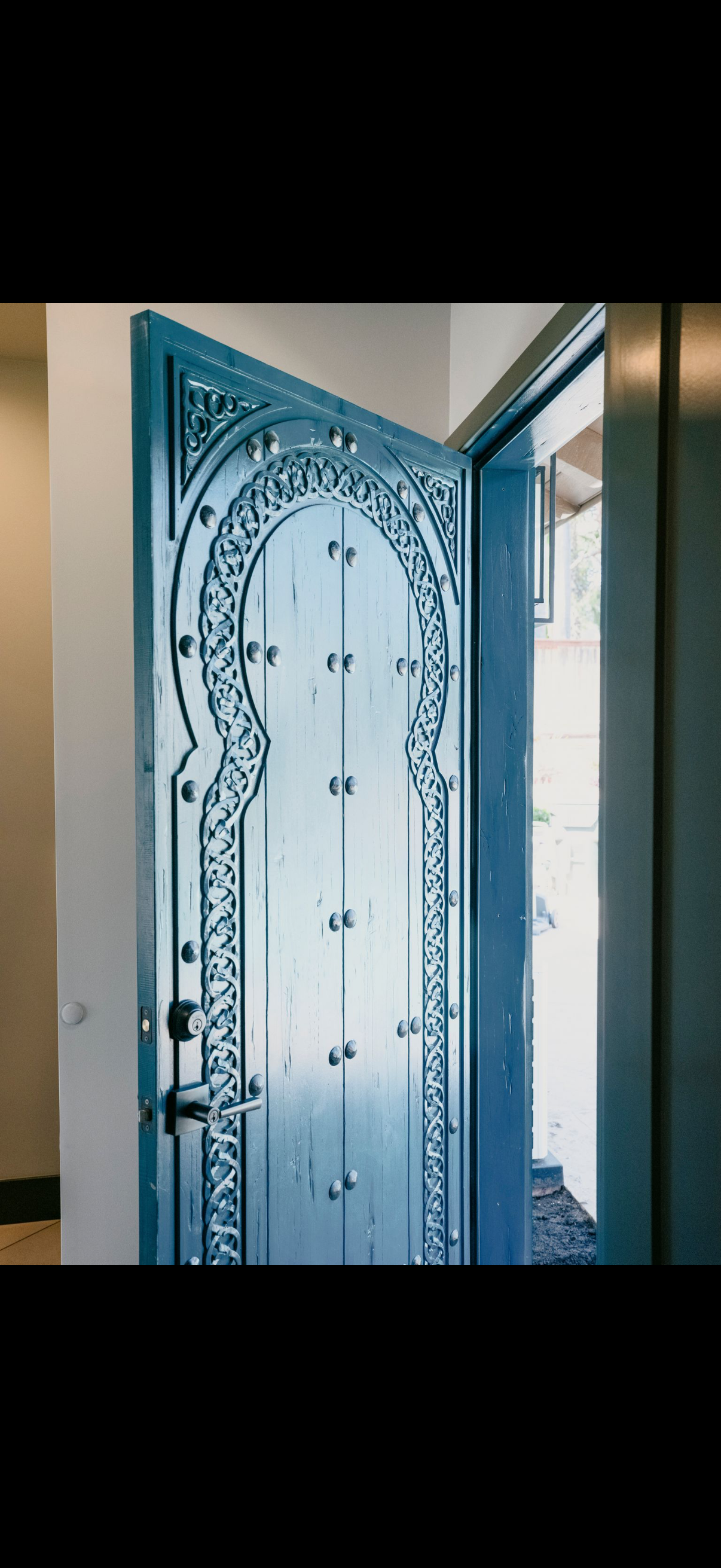 Ornate blue door with decorative carvings, partially open in a white and light-toned room.