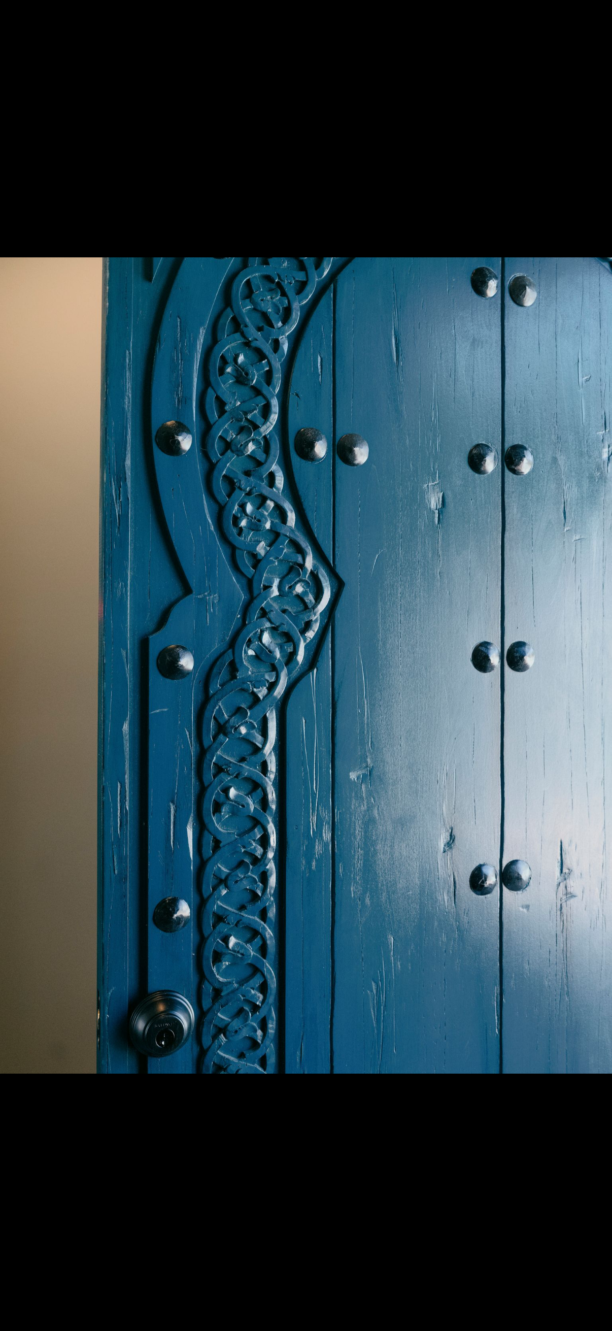Close-up of a weathered blue wooden door with decorative carved details and metal studs.